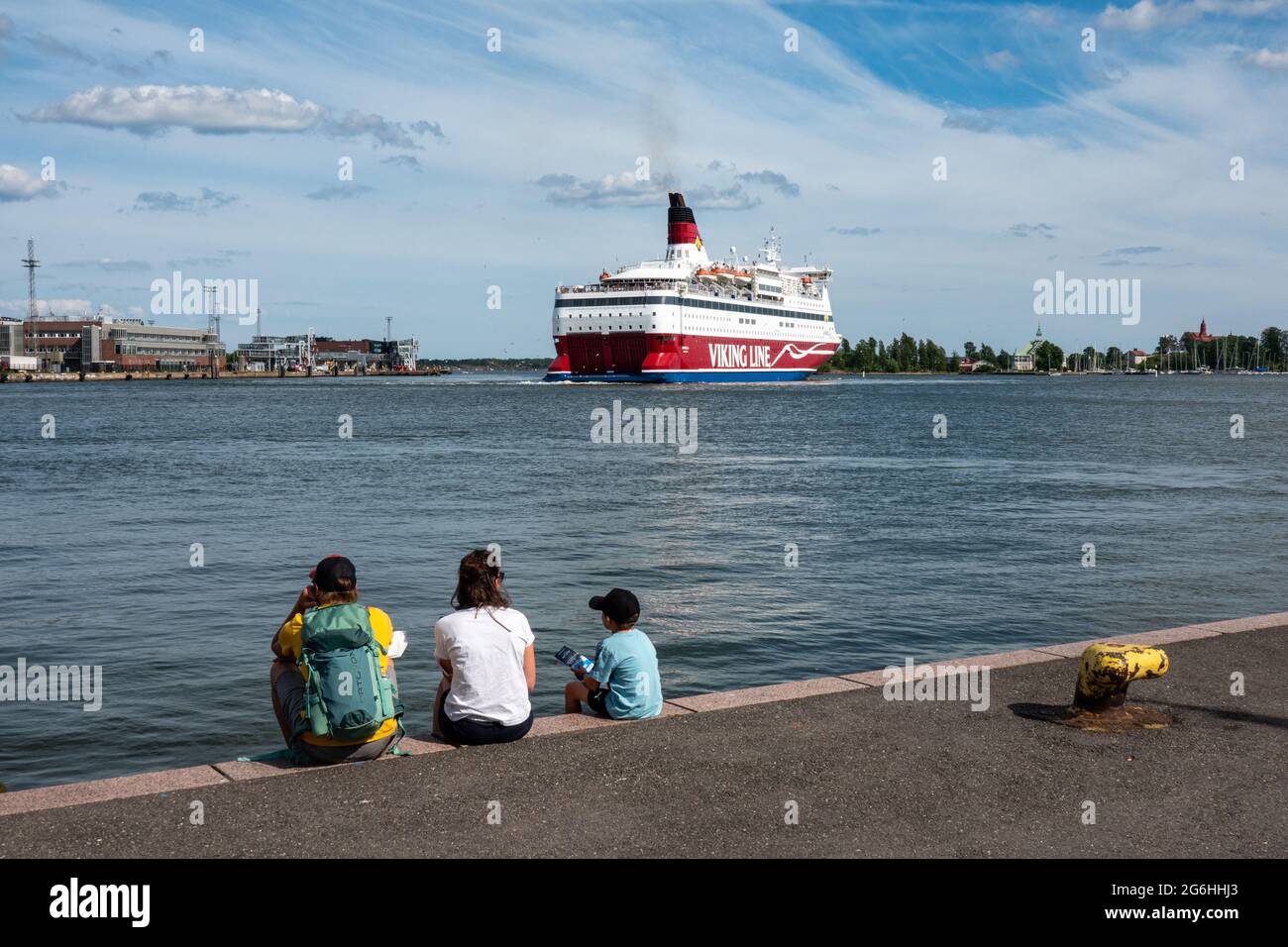 Famiglia di tre persone seduto sul molo di Eteläsatama guardando M/S Gabriella della Viking Line in partenza a Helsinki, Finlandia Foto Stock