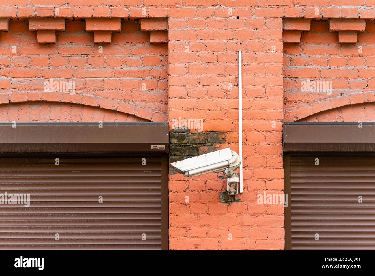 Telecamera di sicurezza montata su una parete in mattoni vicino alle finestre laterali dell'edificio Foto Stock