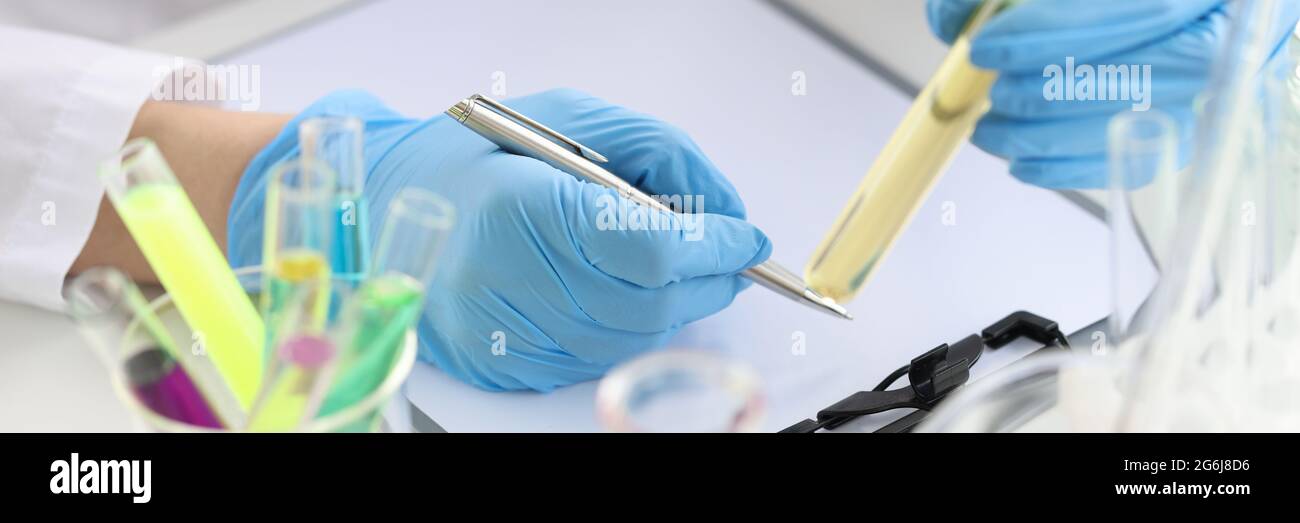 Chimico scienziato che tiene una provetta con liquido giallo nella sua mani e scrittura in primo piano di documenti Foto Stock