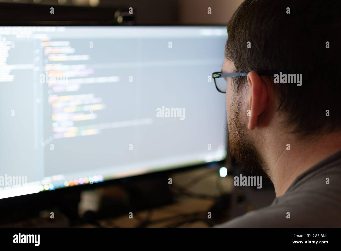 Vista a spalla di un ingegnere software in un codice di debug di ambiente domestico. L'ingegnere ha una barba e degli occhiali. Foto Stock