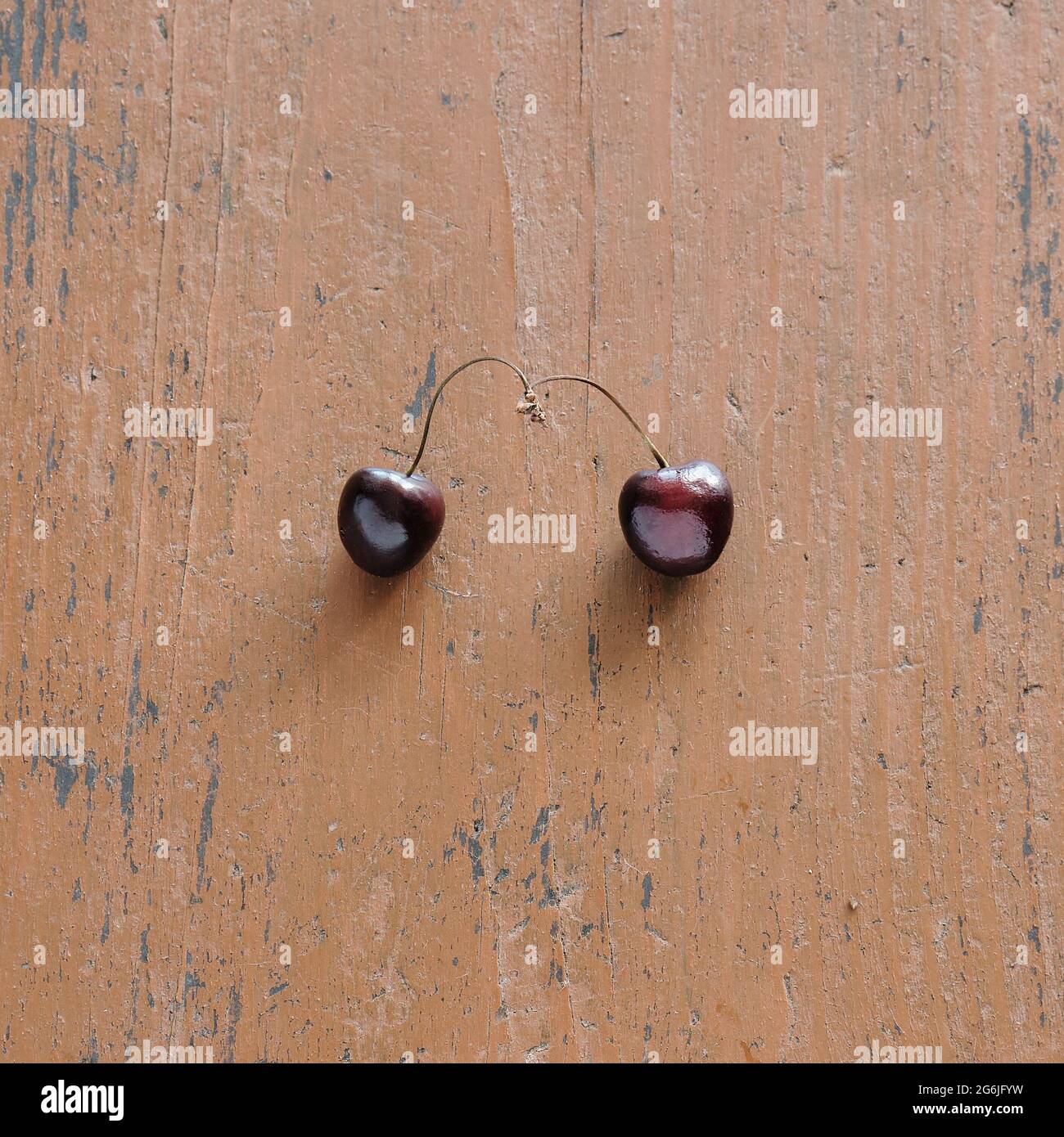 Due ciliegie sul tavolo. Due ciliegie romantiche sono intrecciate con i loro ramoscelli. Foto Stock