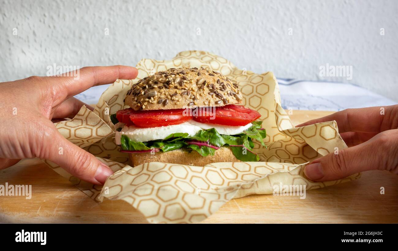 Confezione a due mani con cera d'api riciclabile che avvolge un panino con panino, mozzarella e lattuga. Zero sprechi. Primo piano. Foto Stock