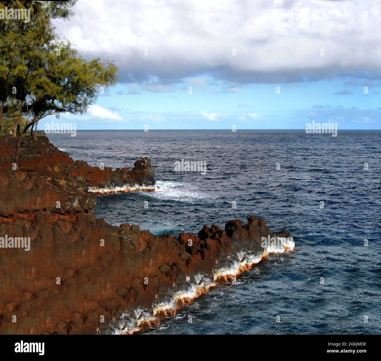 Il Mackenzie state Park, sul lato ventoso della Big Island, è illuminato dalla luce del sole che muore. Scogliere rocciose rosse e acque profonde blu acqua. Foto Stock