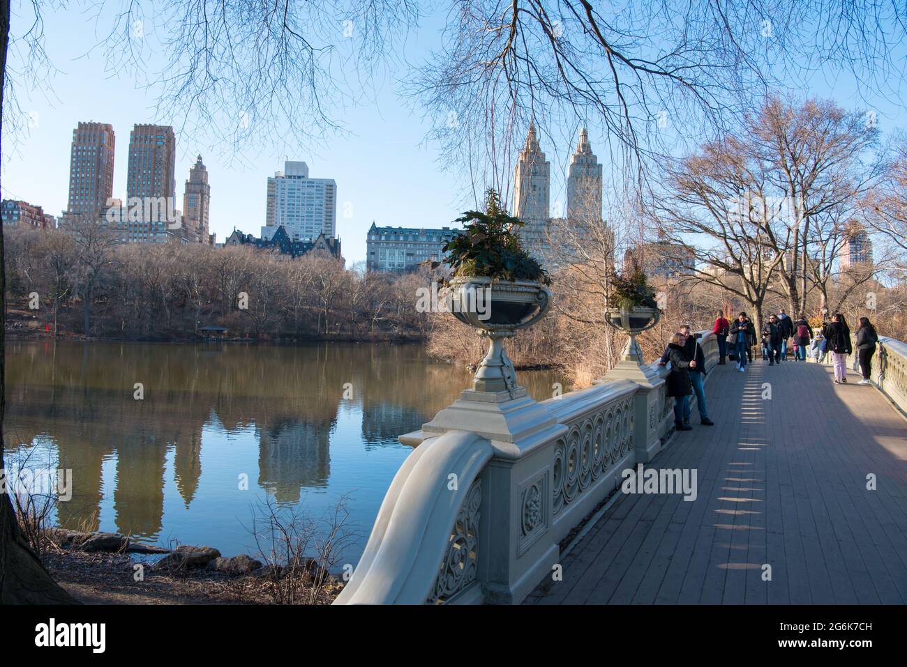 Ponte e lago con raschiatori di cielo sullo sfondo all'interno di Central Park vicino alla casa di barche con le persone che si godono la vista Foto Stock