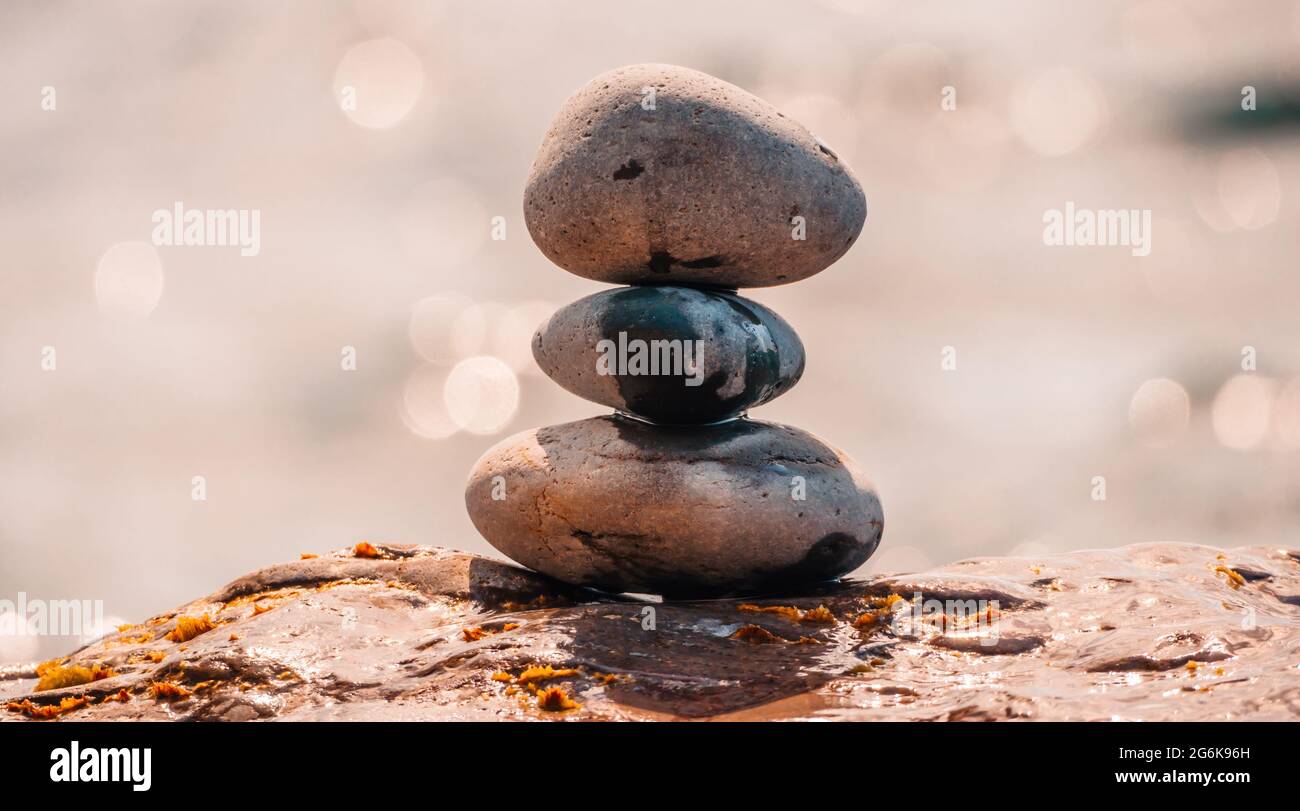 Equilibrata piramide di ciottoli sulla spiaggia in una giornata di sole. Abstract Sea bokeh sullo sfondo. Messa a fuoco selettiva. Pietre Zen sulla spiaggia di mare, meditazione Foto Stock