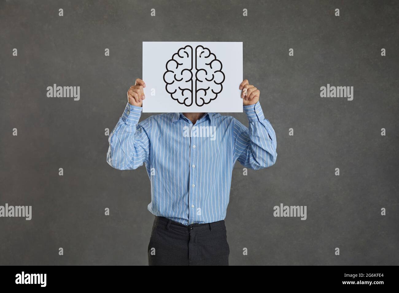 L'uomo creativo copre il suo volto con un foglio di carta con un'immagine di un cervello umano Foto Stock