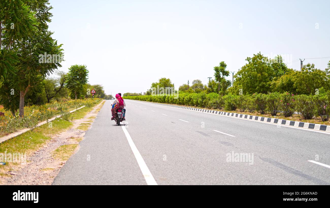 07 luglio 2021 - Reengus, Sikar, India. Lunga strada asfaltata e veicoli che attraversano la foresta. Strada di trasporto asfaltata con boullev verde Foto Stock