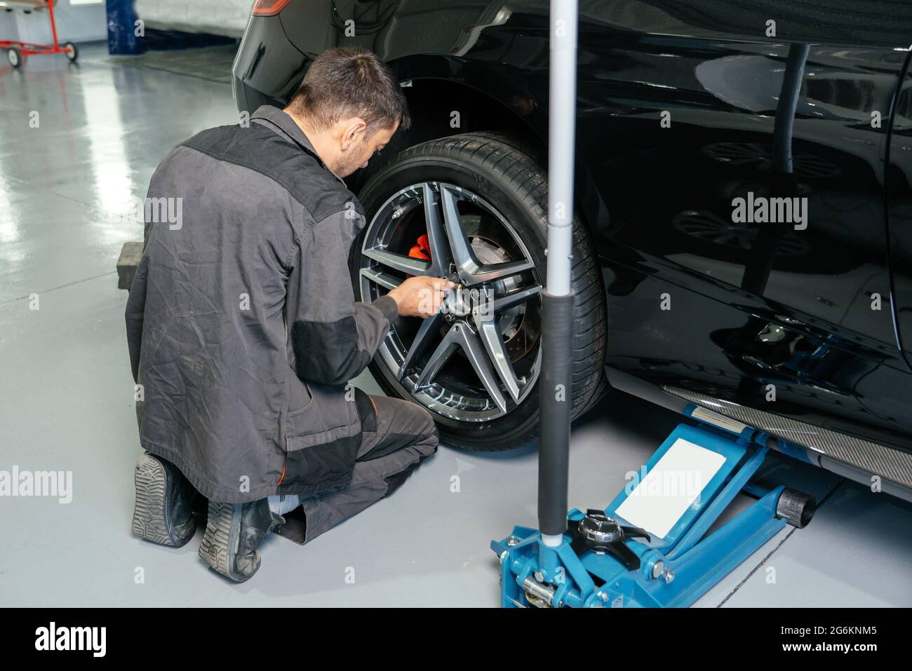 Meccanico che cambia la ruota dell'automobile in officina di riparazione auto usando il martinetto di sollevamento ed il trapano elettrico per allentare i bulloni. Concetto di servizio o di sostituzione. Foto Stock