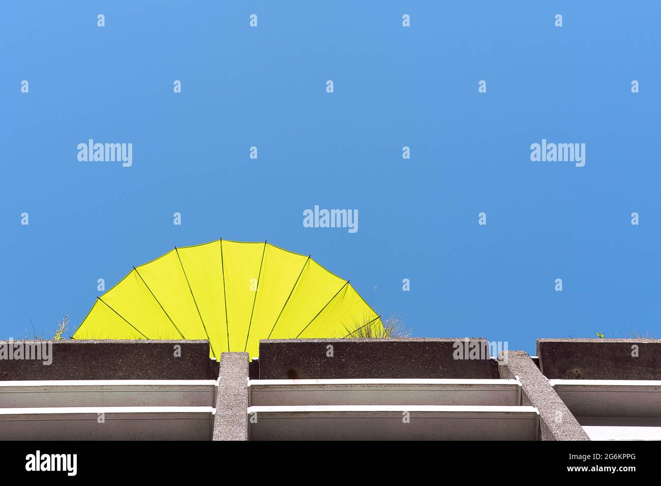 Ombrello giallo sul tetto dell'edificio, vista dal basso. Cielo blu chiaro, parasolo contro il cielo. Foto Stock