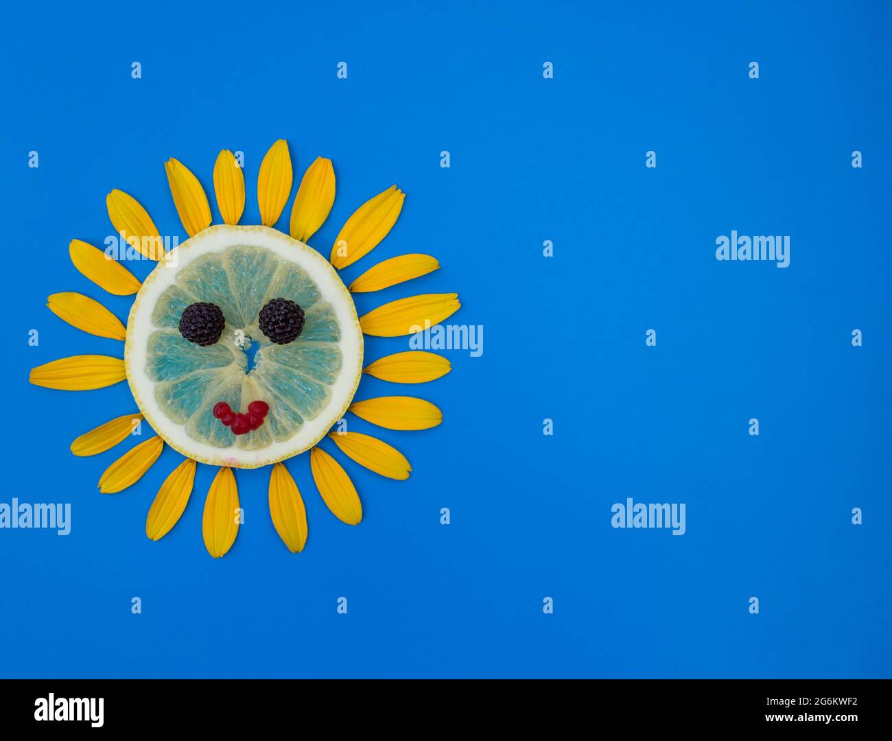 sole disteso da una fetta di limone e petali di fiori gialli intorno su uno sfondo blu. Estate umore gioioso, fantasie floreali, idea creativa. Un simbolo Foto Stock