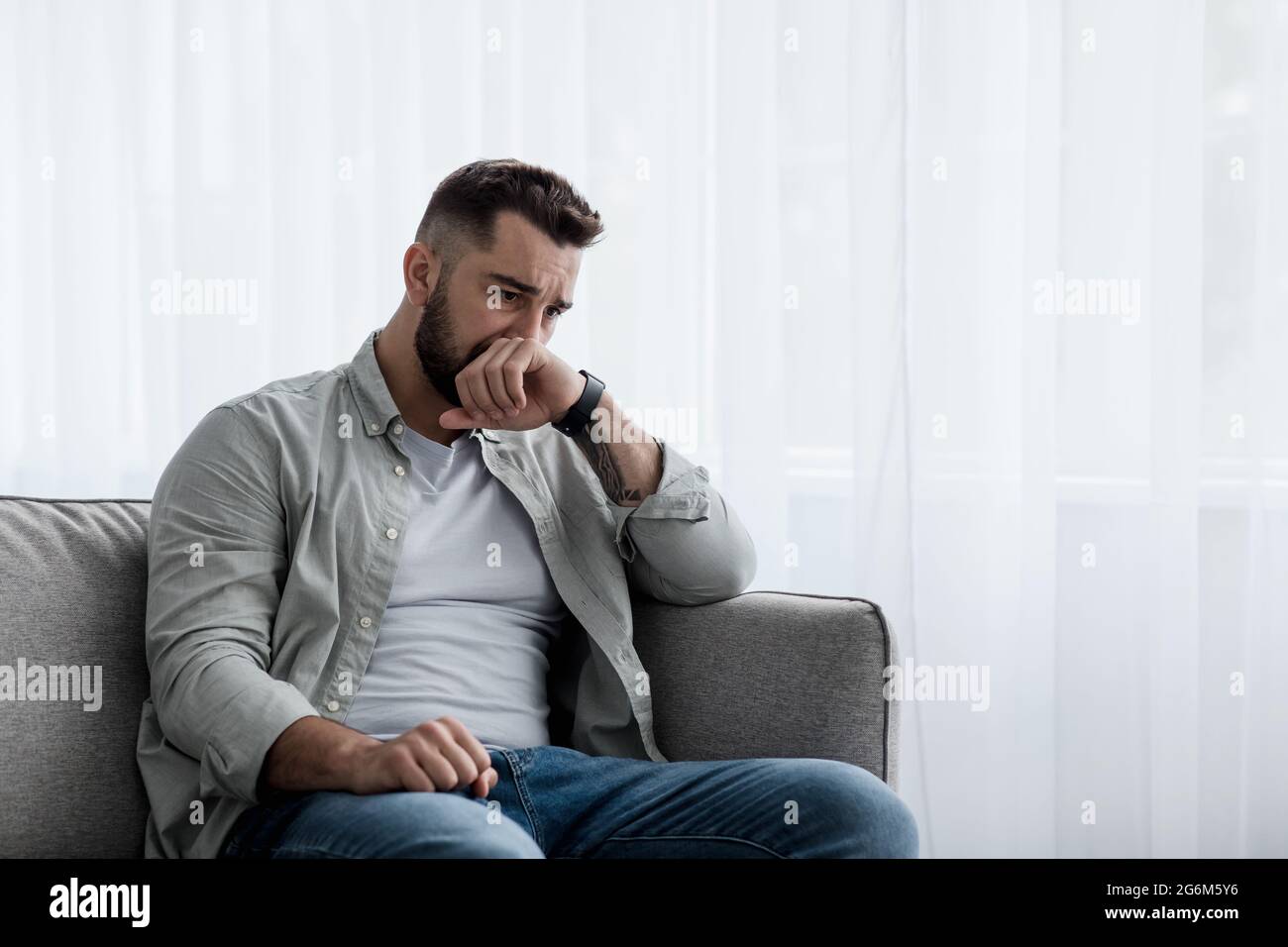 Depresso triste uomo attraente piangendo sul divano a casa, sentendosi solo, stanco e preoccupato Foto Stock