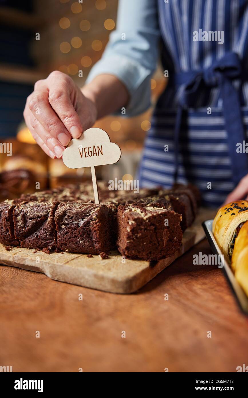 Assistente vendite in panetteria mettere Vegan Label in brownie di cioccolato appena sfornato Foto Stock