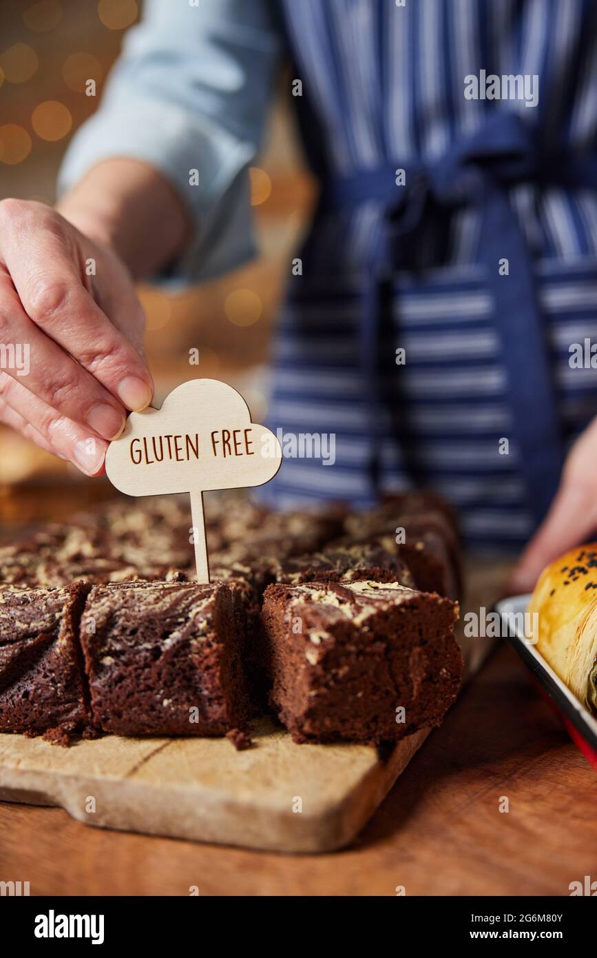 Assistente vendite in panetteria che mette l'etichetta senza glutine in brownie di cioccolato appena sfornate Foto Stock