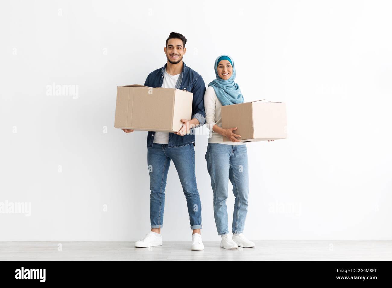 Sorridente coppia musulmana che si sposta in un nuovo appartamento, foto a tutta lunghezza Foto Stock