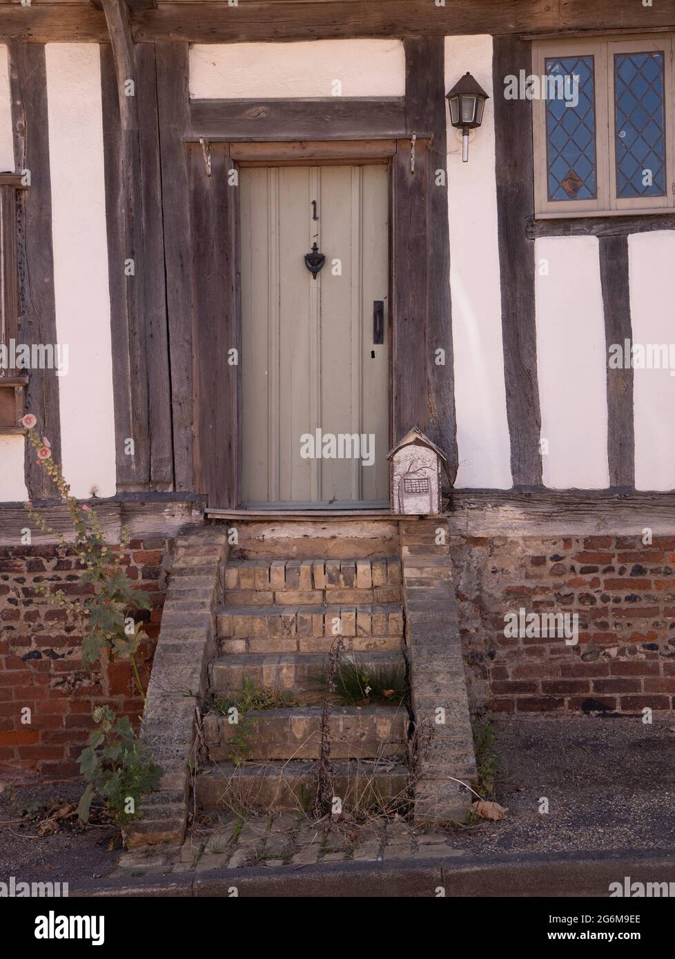 Porta d'ingresso di casa in legno incorniciato con gradini di mattoni troppo grandi e irregolari presso la strada Kersey Sufflok Inghilterra Foto Stock