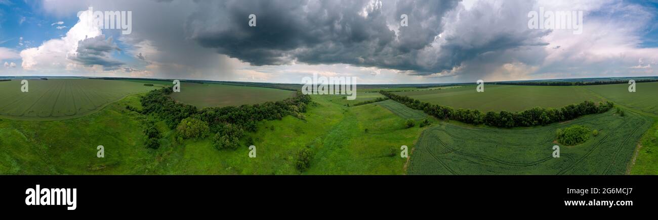 Panorama panoramico aereo vista estiva, volare sopra i campi verdi con il paesaggio torbido nuvoloso. Pioggia oscura condizioni meteorologiche sfavorevoli nella zona agricola rurale. Vista sul drone Foto Stock