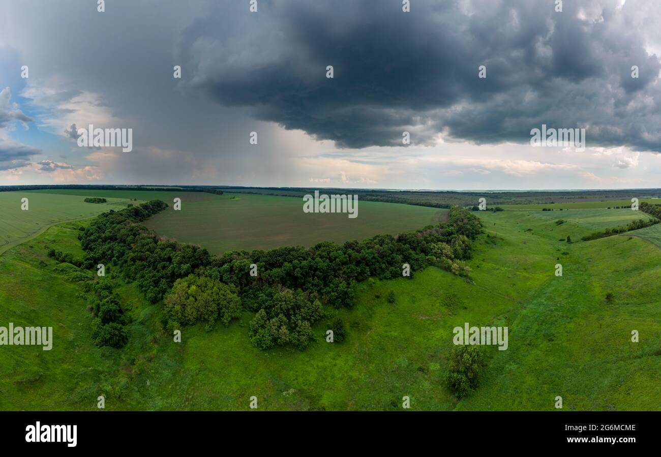 Panorama aereo vista estiva, volare sopra i campi verdi con il paesaggio torbido nuvoloso. Pioggia oscura condizioni meteorologiche sfavorevoli nella zona agricola rurale. Vista sul drone Foto Stock