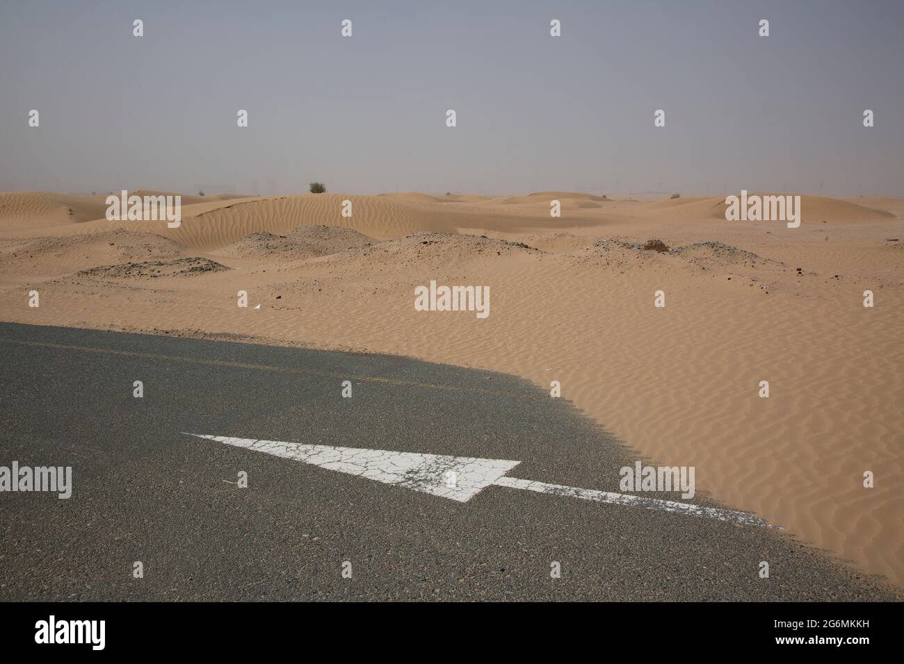 Una freccia bianca sulla strada parzialmente coperta di sabbia a seguito di una tempesta di sabbia a Dubai, Emirati Arabi Uniti. Foto Stock