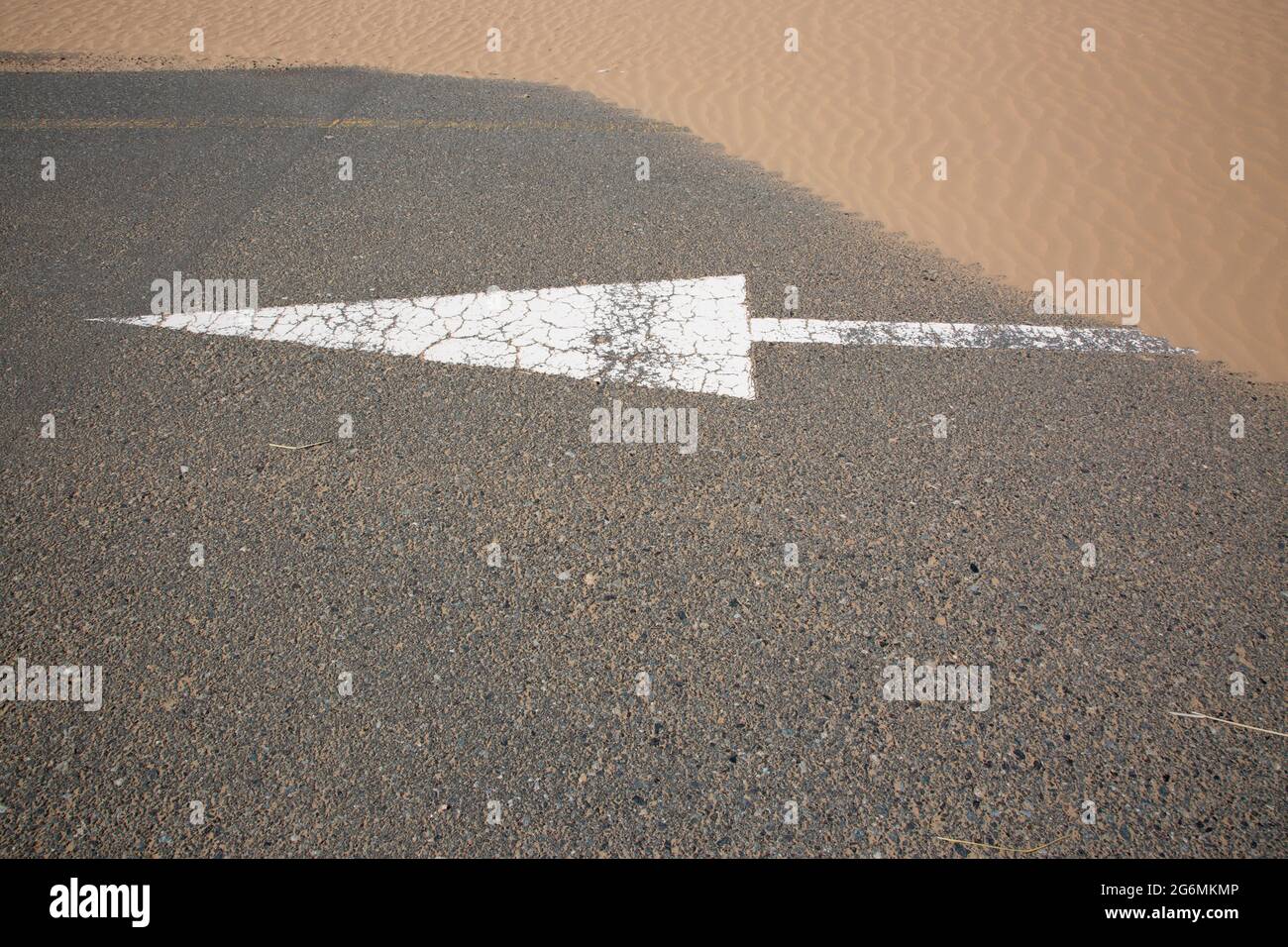 Una freccia bianca sulla strada parzialmente coperta di sabbia a seguito di una tempesta di sabbia a Dubai, Emirati Arabi Uniti. Foto Stock