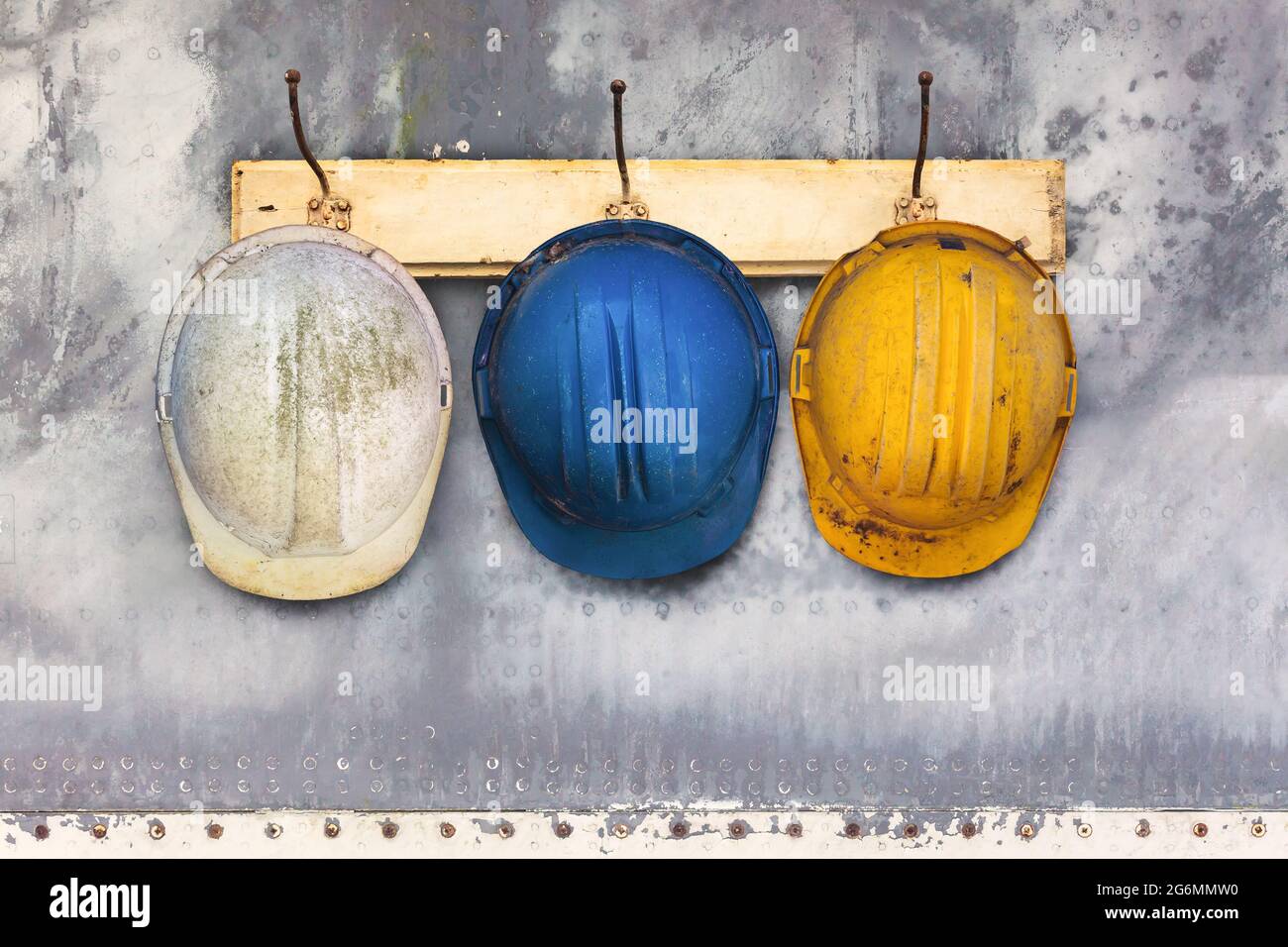 Tre caschi da costruzione appesi su una vecchia rastrelliera in legno Foto Stock