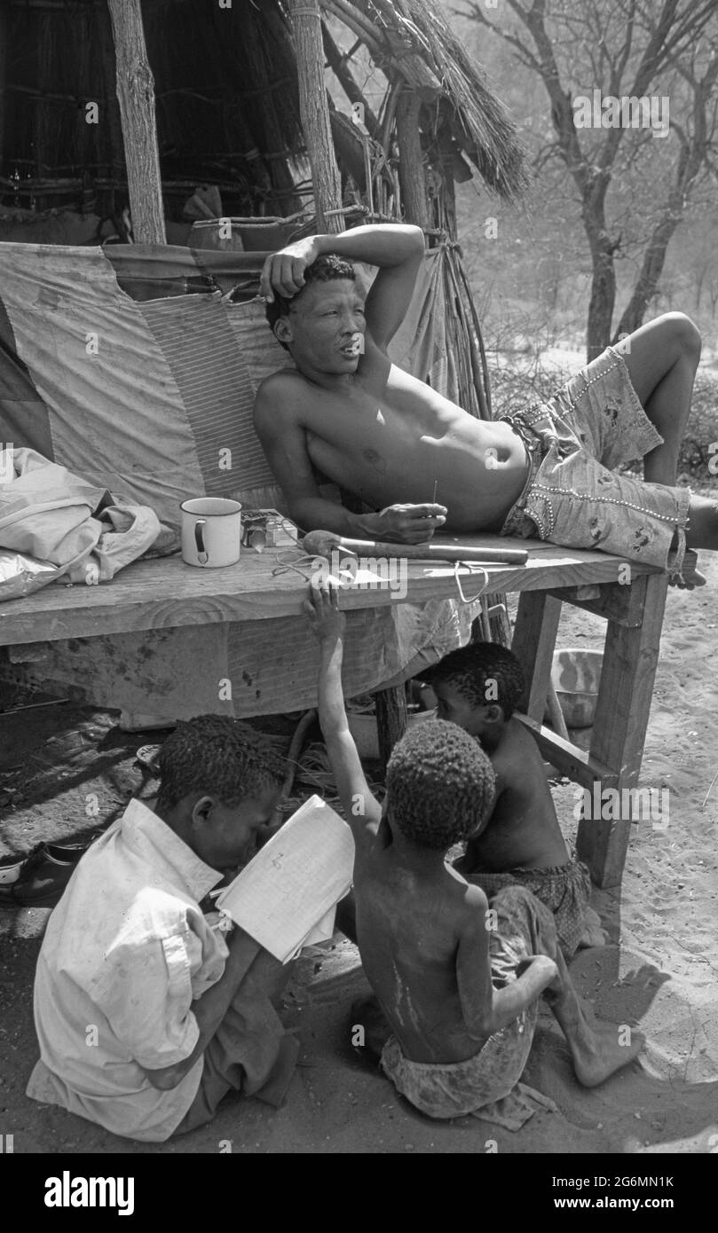 Botswana: Un campo di boscimani con semplici capanne sulle colline di Tsodillo, nel Kalahari centrale, dove un boscimano e i suoi figli stanno rifacendo e giocando Foto Stock