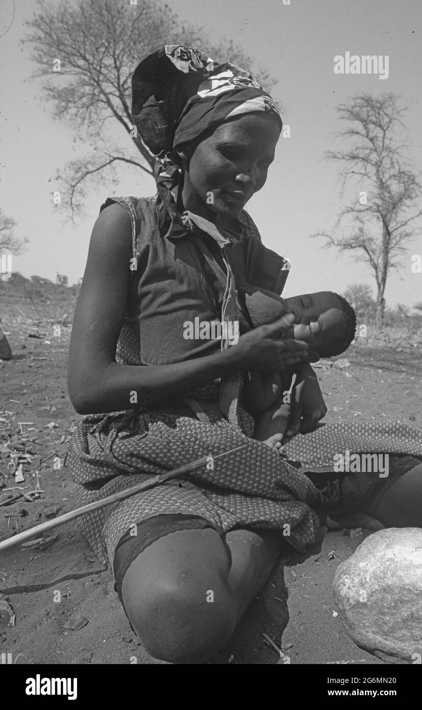 Botswana: Una donna di san con il suo bambino che crea arte dei boscimani dalle uova di struzzo alle colline di Tsodillo nel delta dell'Okavango all'interno del Kalahari centrale Foto Stock
