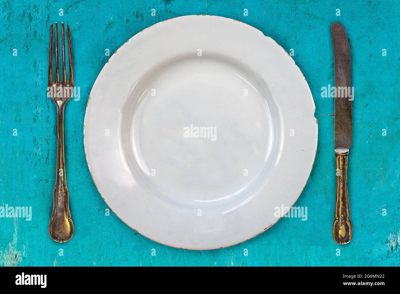 Immagine in stile retrò di un piatto vuoto con forchetta e coltello su sfondo blu Foto Stock