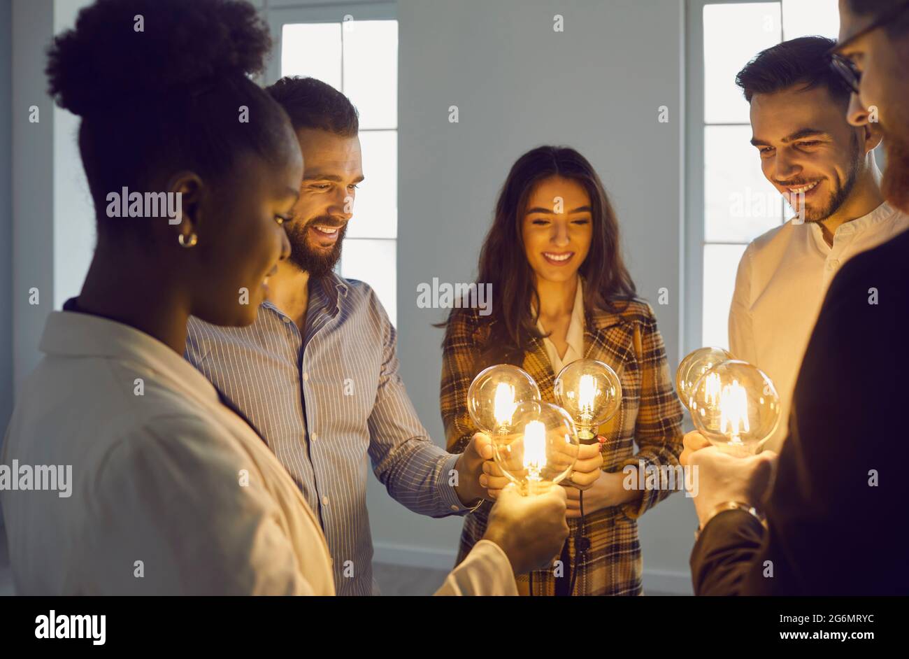 Uomini d'affari multirazziali che tengono una lampadina luminosa che unisce la lampada Foto Stock