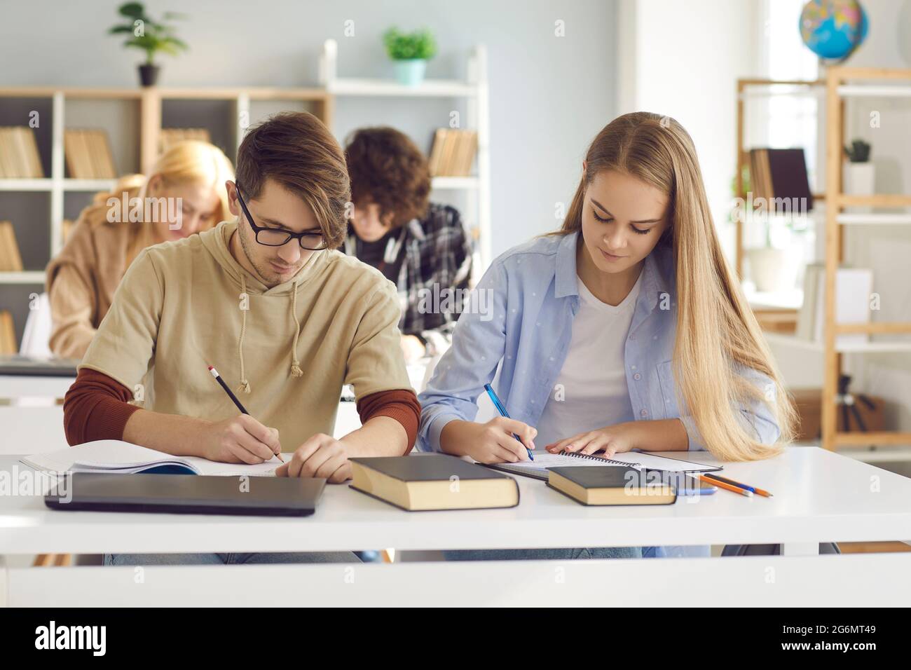 Diversi studenti alla scrivania condivisa che fanno appunti per studiare insieme all'università Foto Stock