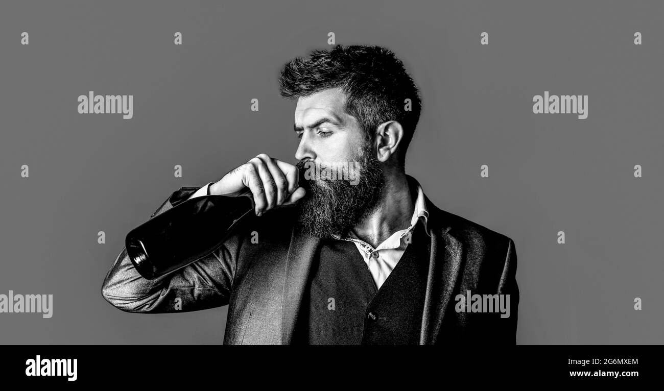 La persona tiene in mano una bottiglia di vino rosso. Uomo bearded con una bottiglia di champagne e un bicchiere. Elegante uomo in smoking, tuta, giacca. Bianco e nero Foto Stock