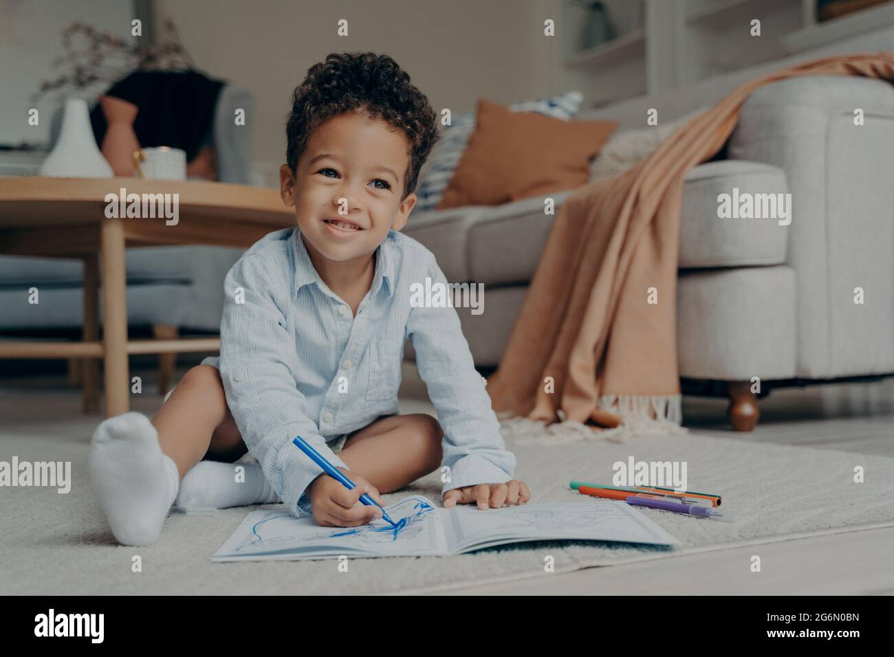 Piccolo ragazzo afro seduto sul pavimento e disegnando con colorati pennarelli punta Foto Stock