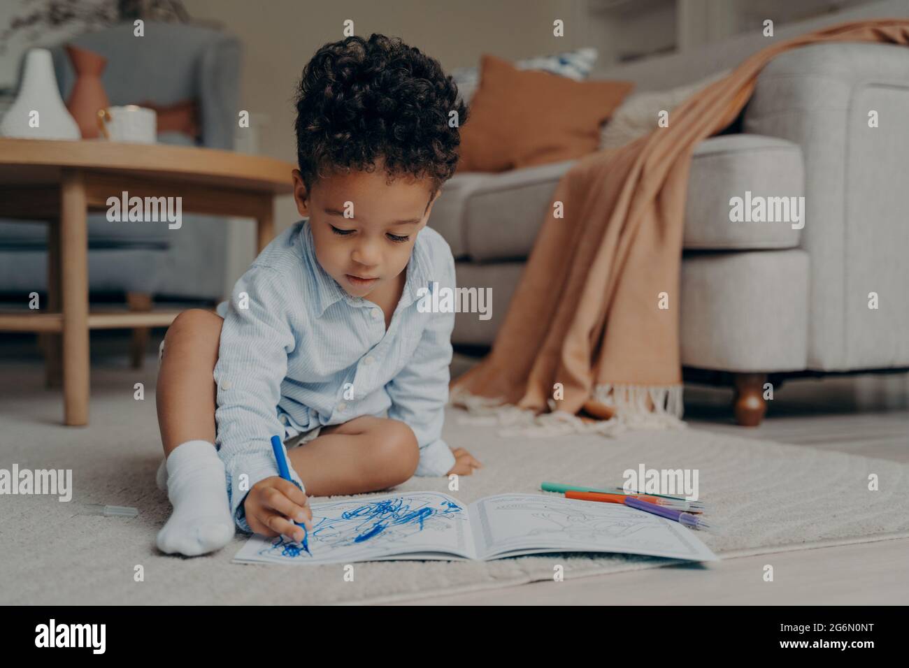 Piccolo bambino africano seduto sul pavimento e disegnando con penna blu con punta in feltro Foto Stock