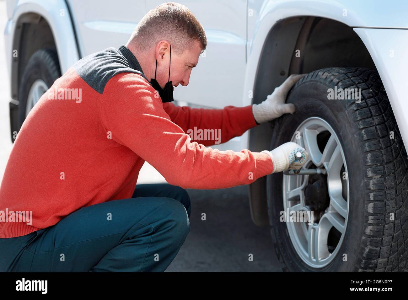Un uomo cambia una ruota su un'auto sulla strada in una giornata di sole. Guida su strada con una foratura degli pneumatici. Foto Stock
