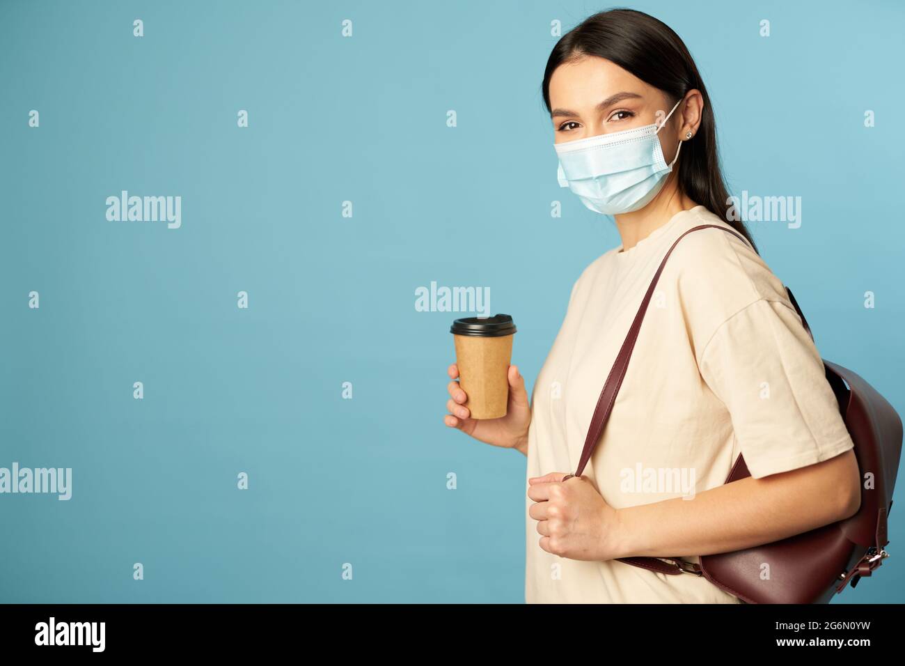 Bella signora in una maschera usa e getta con una bevanda calda in mano Foto Stock