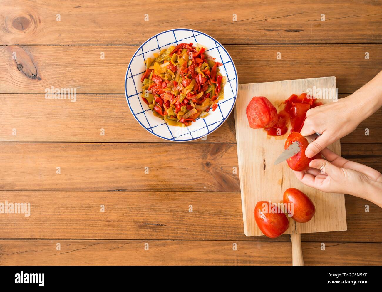 Dettaglio delle mani di una donna che spellano i pomodori con un coltello. Preparazione di peperoni arrostiti, un piatto tipico della cucina spagnola e andalusa. Foto Stock