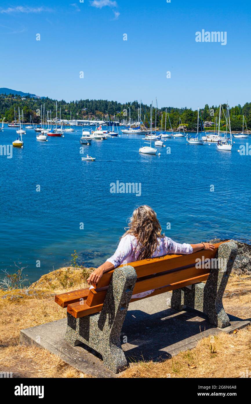 Donna con capelli biondi e mousse seduta su una panchina che guarda su Shoal Harbour a Sidney British Columbia Canada Foto Stock