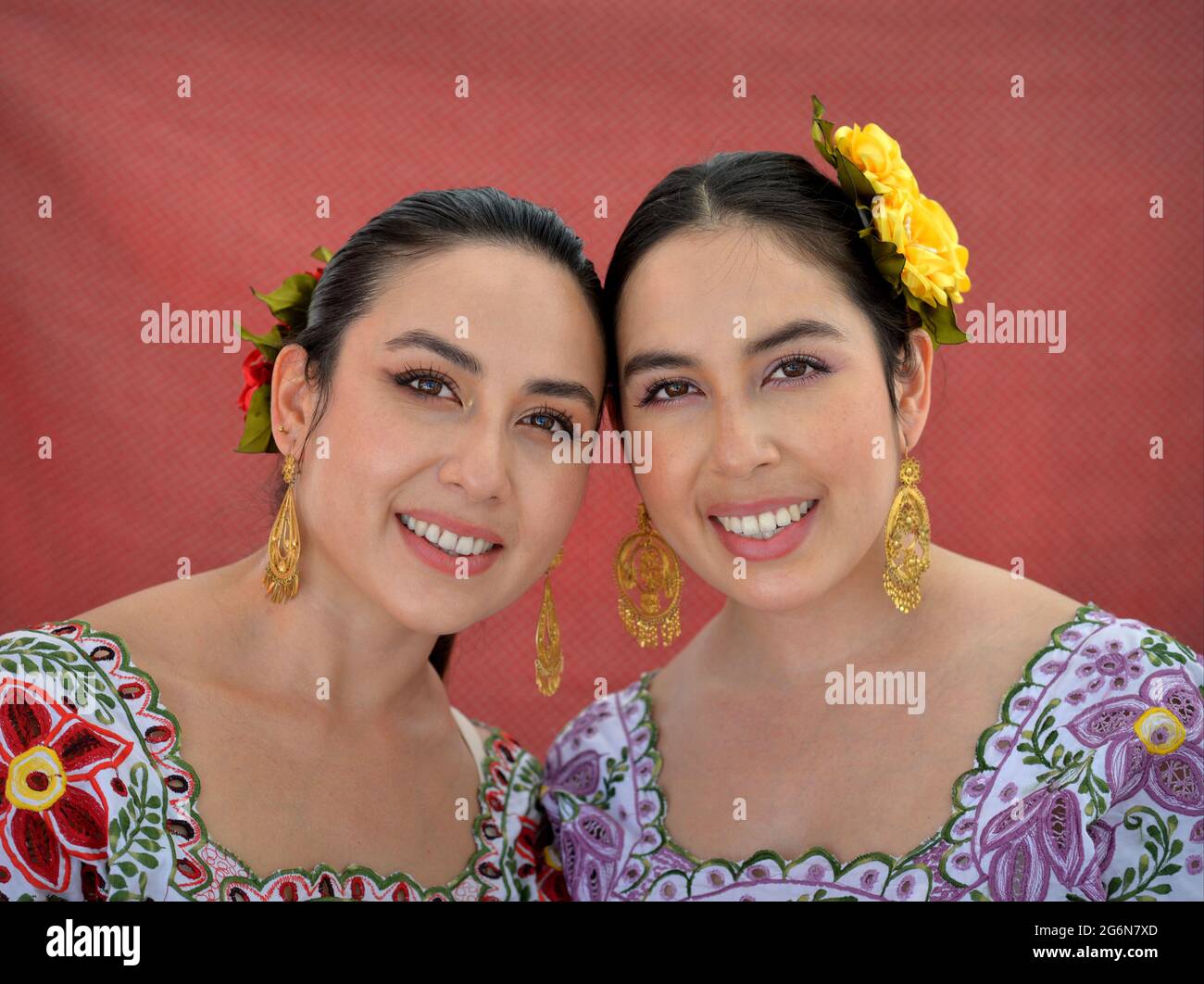 Belle sorelle messicane Yucatecan gemelle con occhio trucco indossare tradizionale Yucatecan vestito con fiori nei loro capelli e sorriso per la macchina fotografica. Foto Stock
