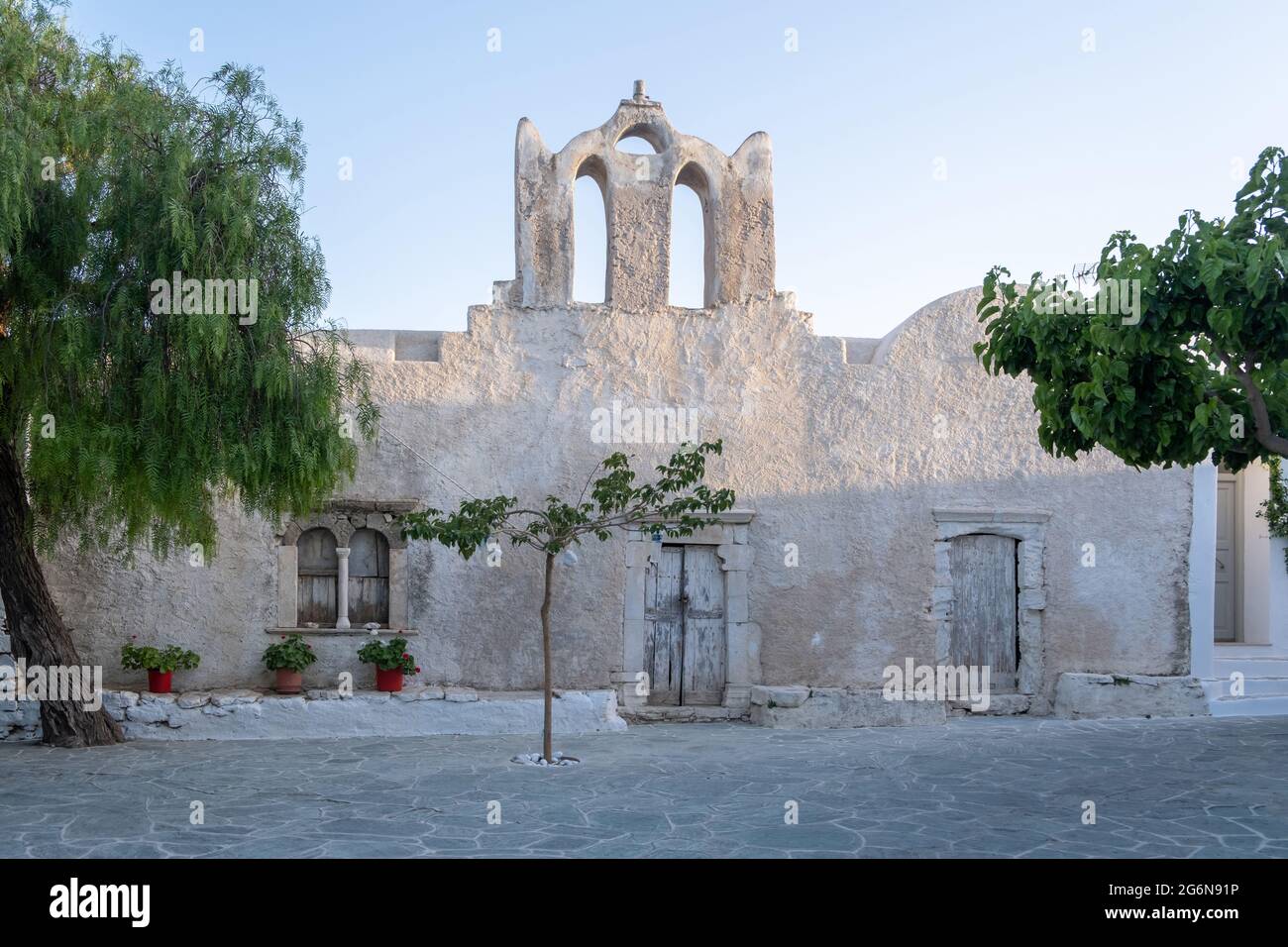 Grecia, Cicladi. Isola di FOLEGANDROS, vecchia chiesa nella piazza del villaggio di Chora. Tradizionale cappella delle Cicladi, pareti e alberi imbiancati, cielo blu chiaro bac Foto Stock