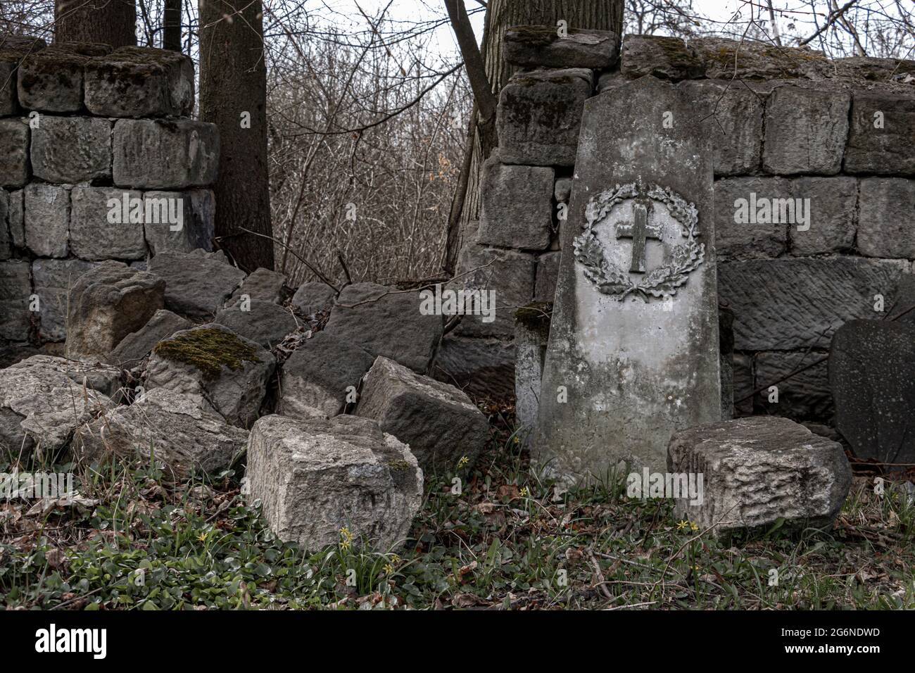 Un muro di pietra demolito con una lapide danneggiata in un cimitero Foto Stock