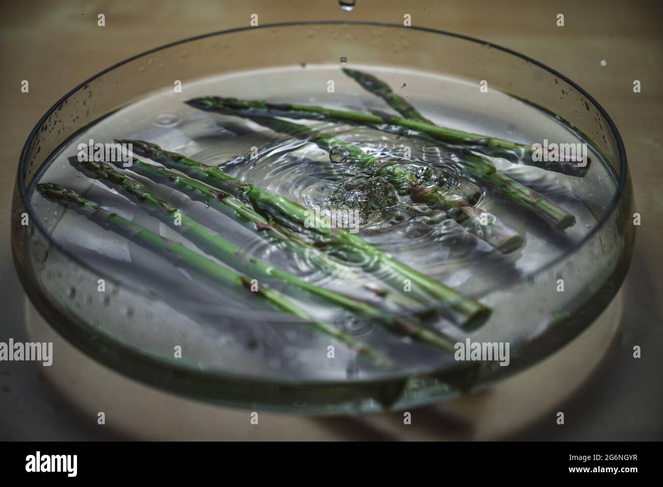 Lavaggio ad acqua di asparagi in caduta. Asparagi in una ciotola di acqua spruzzata. Verde comprato al mercato del coltivatore. Cibo ad alto contenuto di vitamine. Foto Stock