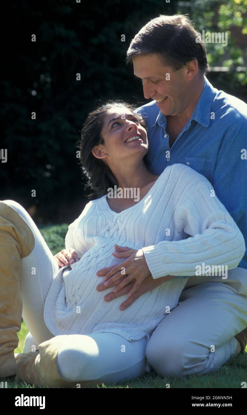 donna incinta anglo-asiatica molto incinta seduta fuori con il suo compagno Foto Stock
