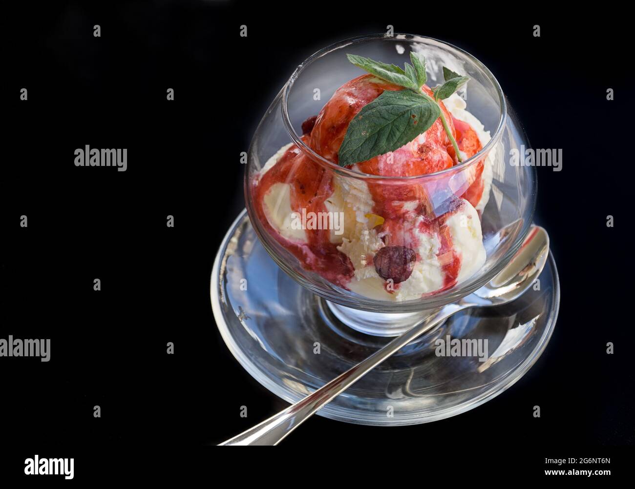 Gelato alla vaniglia con fragole, smalto di frutta e foglie di menta in un recipiente di vetro su sfondo nero. Spazio di copia. Foto Stock