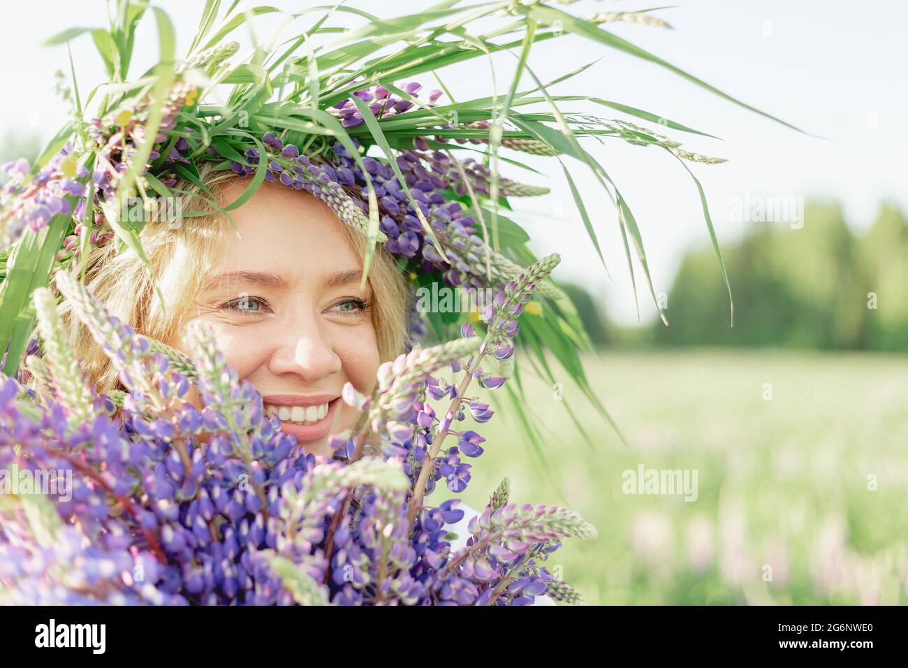 Una ragazza hippy che tiene bouquet di fiori selvatici nelle sue mani. La ragazza nascose il viso dietro un bouquet di lupini. La ragazza tiene il bouquet grande di lupini viola in un Foto Stock