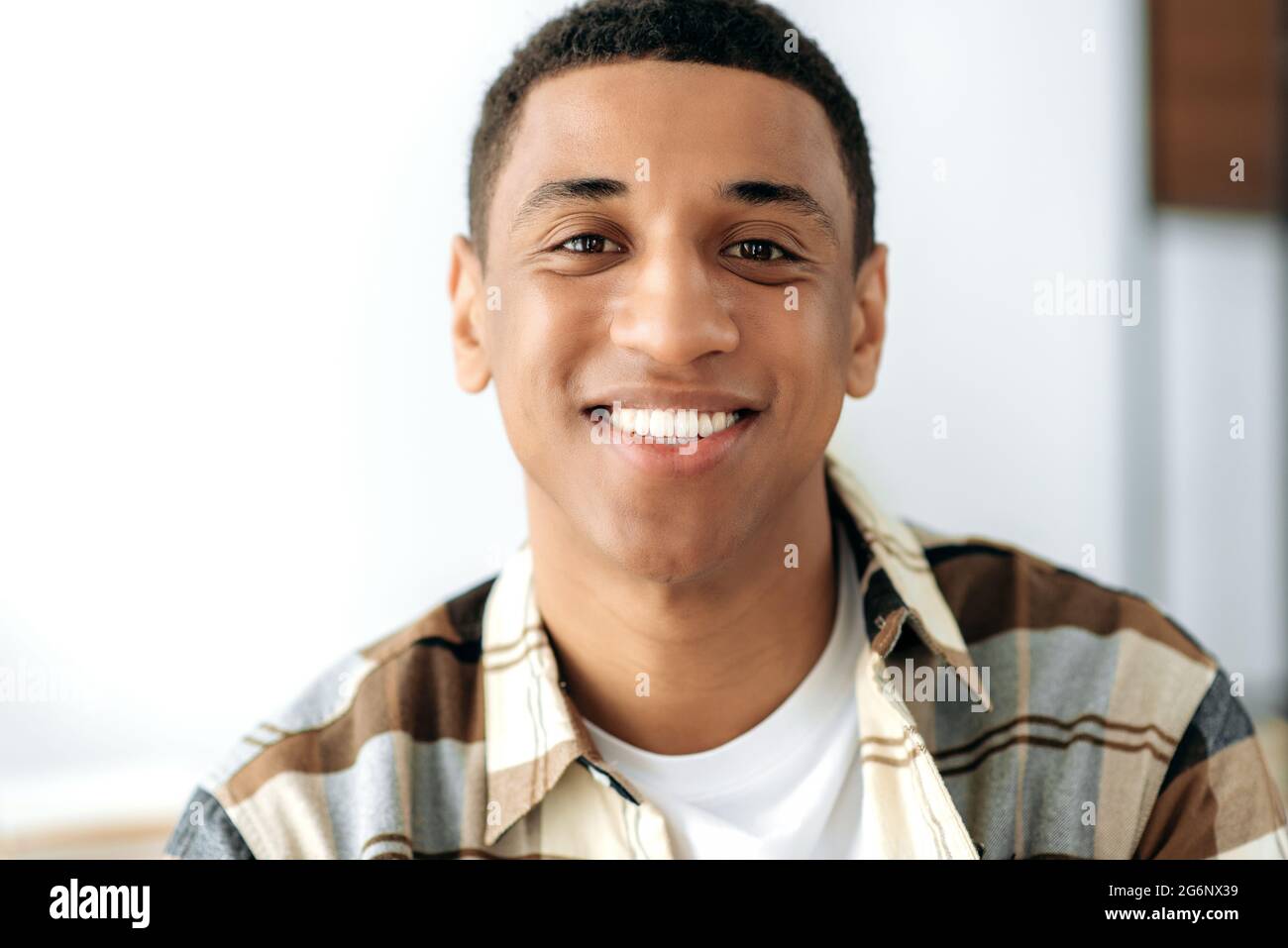 Positivo gara mista giovane uomo. Primo piano di un bel ragazzo latino millenario soddisfatto con, freelance, designer creativo o studente, in piedi in casa, guardando direttamente la fotocamera, sorridente amichevole Foto Stock