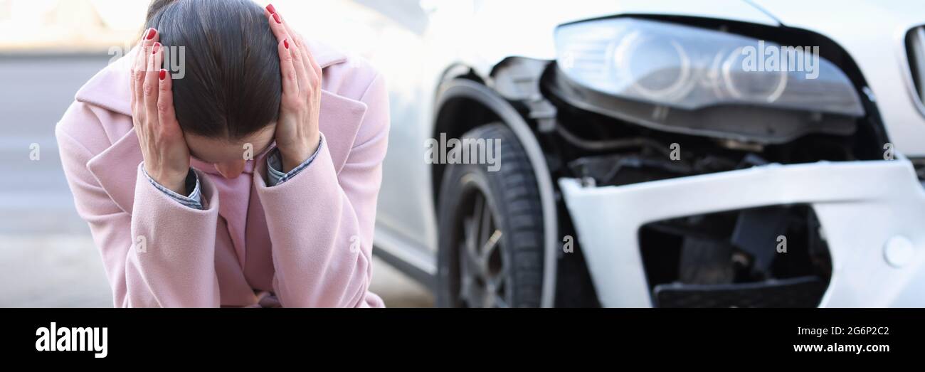 Una donna turbata si siede con la testa giù accanto a. auto sviluppata Foto Stock