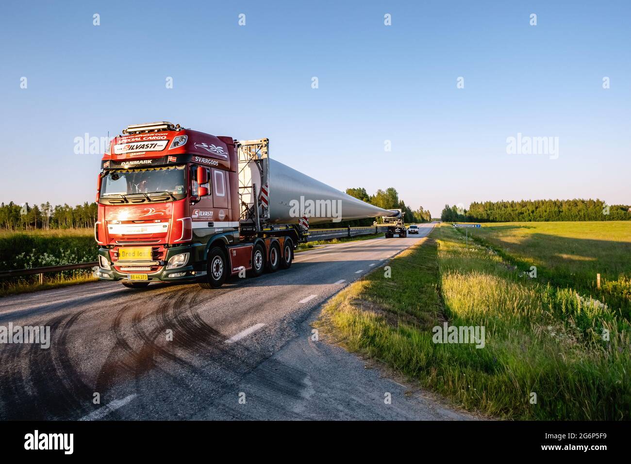 UMEA, SVEZIA - 04 luglio 2021: Trasporto di una pala ad elica molto lunga su piccola strada di campagna. Moderno trattore autostradale, scortato Foto Stock