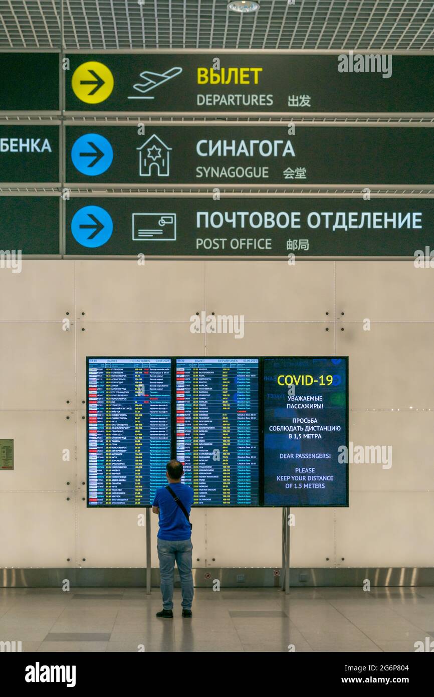 La persona si trova di fronte all'esposizione con voli e informazioni sul covid nel terminal dell'aeroporto, sotto le indicazioni per la sinagoga e l'ufficio postale, DME, Mosca, Russ Foto Stock