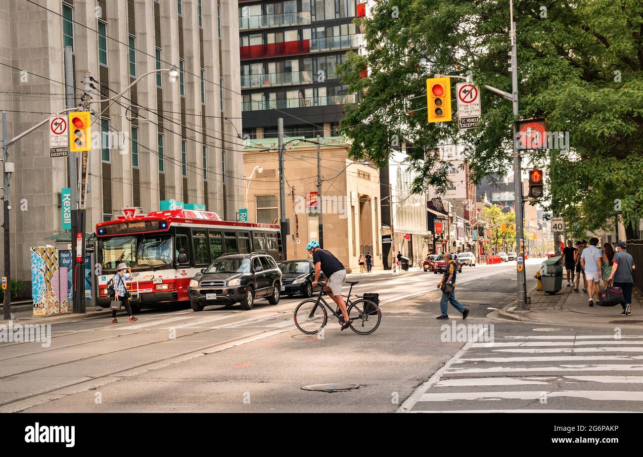 TORONTO, CANADA - 06 05 2021: Traffico su Queen Street all'incrocio di University Avenue nel centro di Toronto con un ciclista in primo piano e TTC Foto Stock