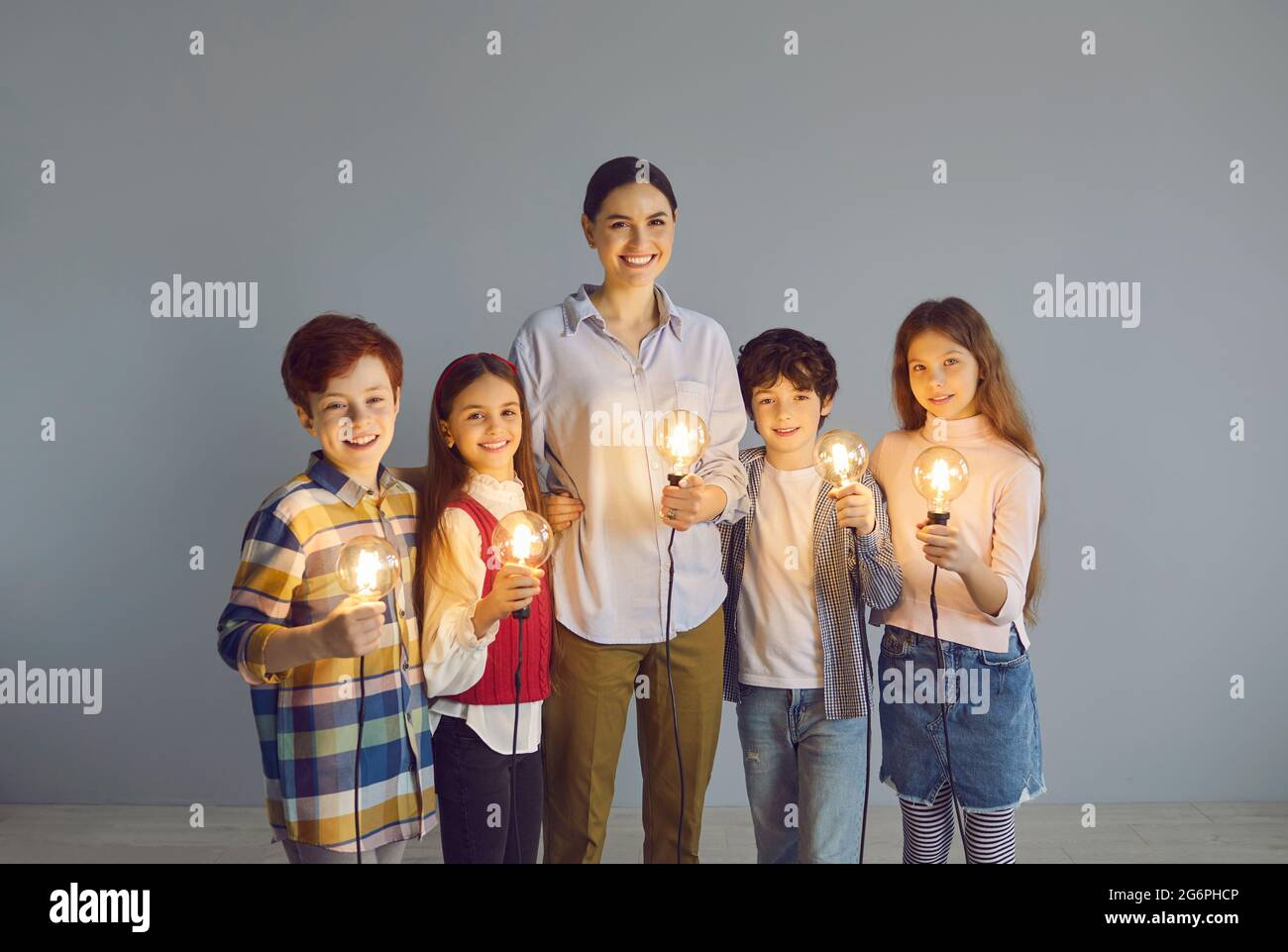 Ritratto di gruppo di felice insegnante di scuola e dei suoi studenti creativi che tengono lampadine Foto Stock