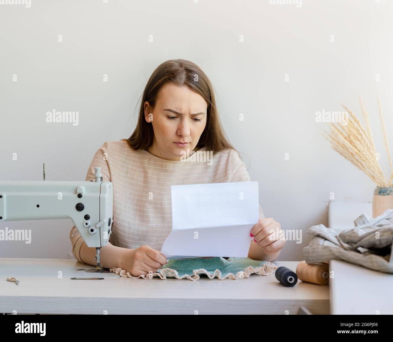 Giovane buisnesswoman turbato quando legge la fattura di imposta mentre sedendosi al suo proprio atelier di moda Foto Stock